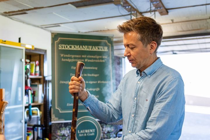 Staatssekretär Sebastian Thul mit einem Wanderstock vor dem Schild der Stockmanufaktur